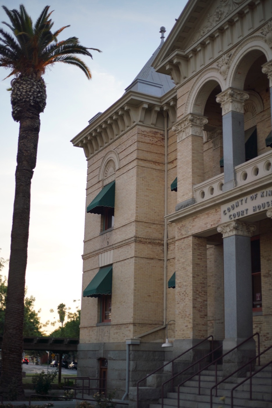 The Kings County Court House in Hanford: tan brick, arched porch openings, and a tall palm tree beside it